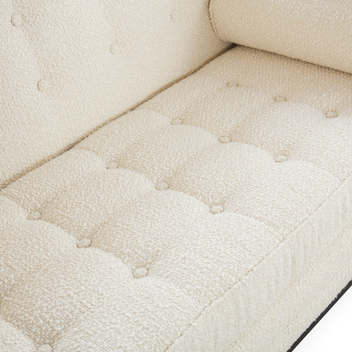 Close-up of a cream bouclé upholstered sofa seat with tufted button details and a matching back cushion.