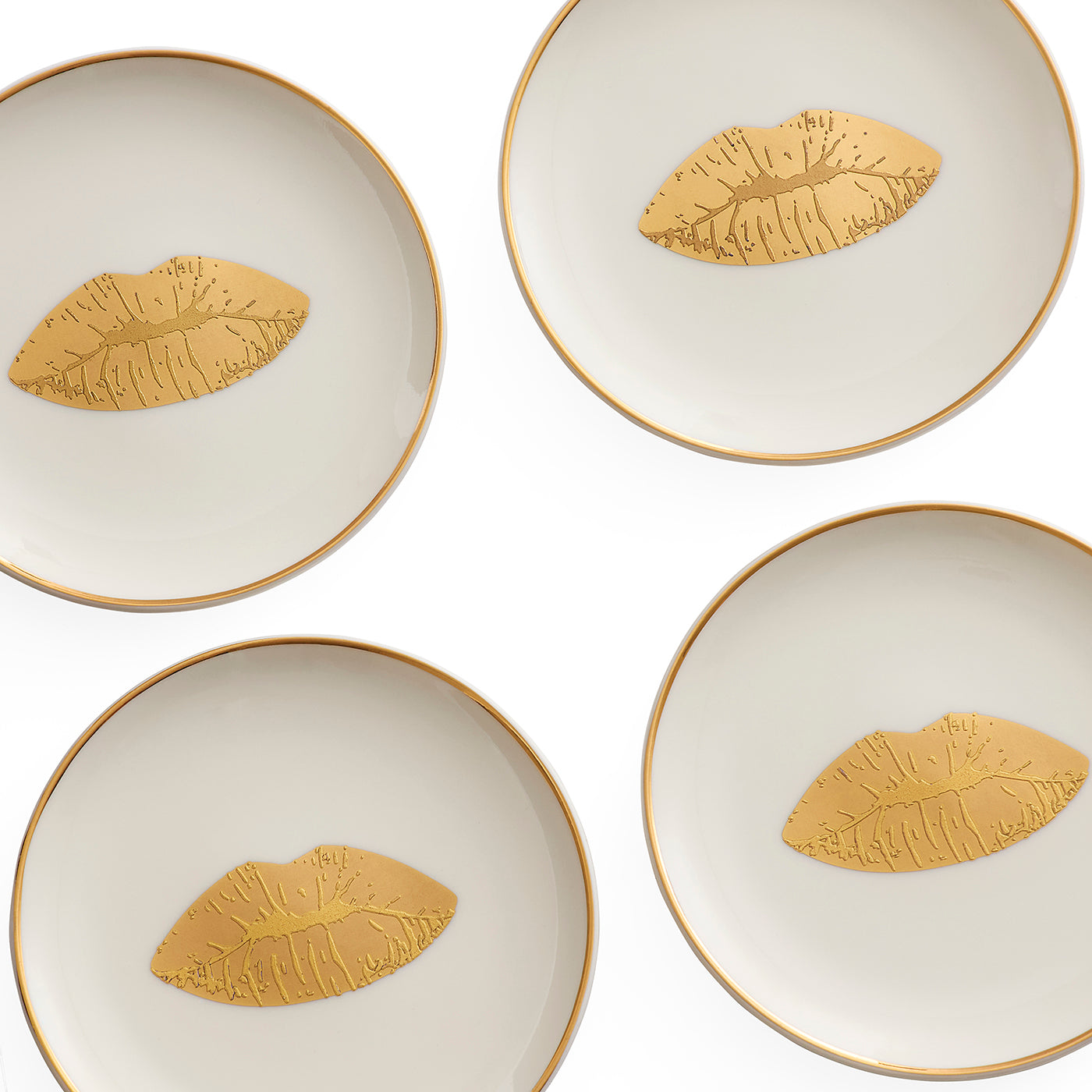Four round white ceramic plates with gold rims, each decorated with a gold metallic lip motif in the center, arranged in a grid on a white background.