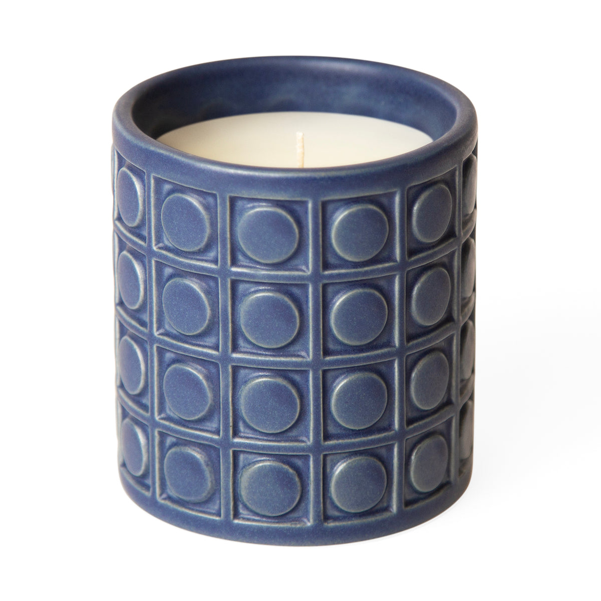 A blue ceramic candle holder with a textured embossed grid pattern of squares and circles, containing a white wax candle with a single wick, set against a plain white background.