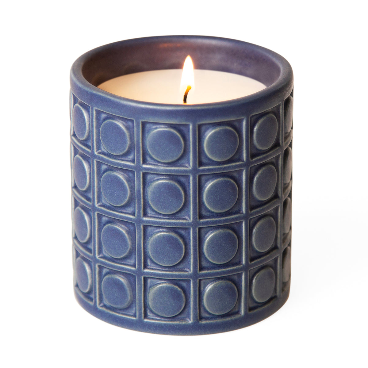 A lit scented candle in a dark blue textured ceramic holder with a raised geometric grid pattern, set against a plain white background.