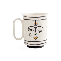 A white ceramic mug with a handle, decorated with minimalist black line art of a face and small gold accents, set against a plain white background.
