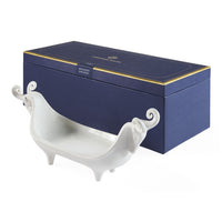 White decorative dish with curved handles in front of a blue box with gold accents