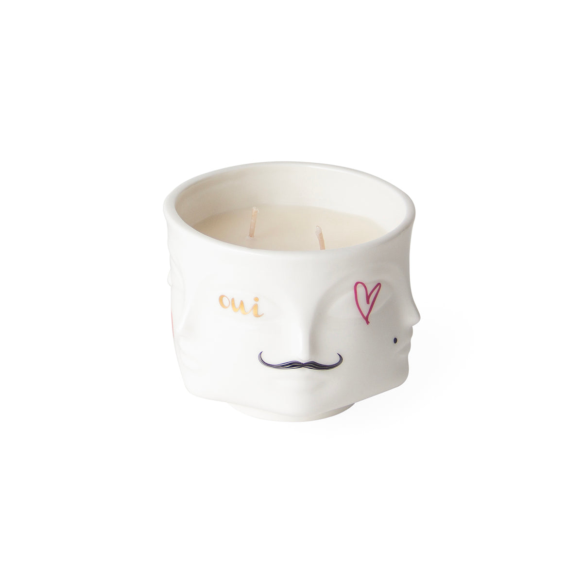 A white ceramic candle holder shaped like a stylized face, featuring a gold 'cui' on one eye, a pink heart on the other eye, and a black mustache. The candle is filled with cream-colored wax and has two visible wicks, set against a plain white background.