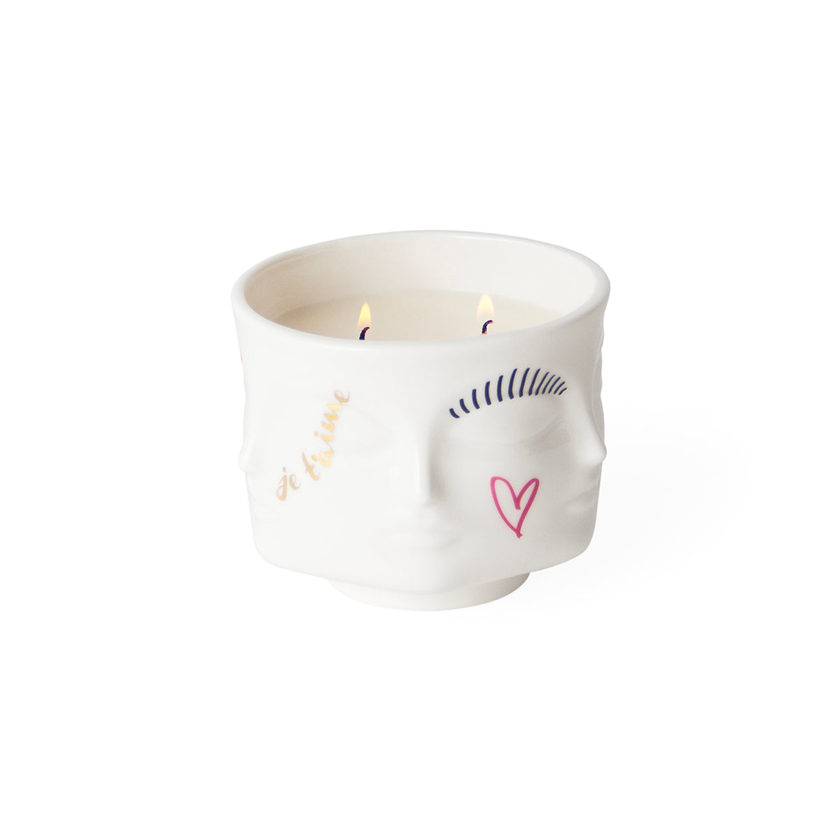 A white ceramic candle holder shaped like a stylized face, with two lit candles inside. The face features minimalist hand-drawn style illustrations in gold, navy blue, and pink, including the words 'Be Kind' in gold script.
