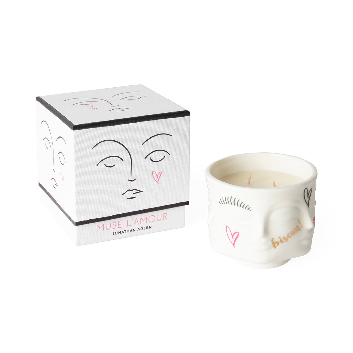A white ceramic candle jar with a sculpted face design and pink heart details, shown next to its white cube-shaped packaging box featuring minimalist face line art.