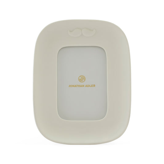 A cream-colored picture frame with a small mustache detail at the top and gold 'JONATHAN ADLER' branding in the center, shown on a plain white background.