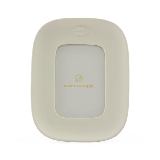 Jonathan Adler picture frame in a warm cream color with a gold logo and a subtle lips icon at the top, shown on a clean white background.