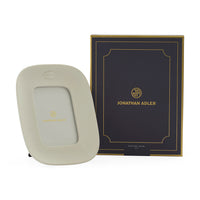 A cream-colored Jonathan Adler picture frame with a gold logo, shown next to its black and gold branded presentation box on a white background.
