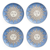 Four round ceramic plates arranged in a 2x2 grid, each featuring a light blue background with a stylized sun face design in white and gray.