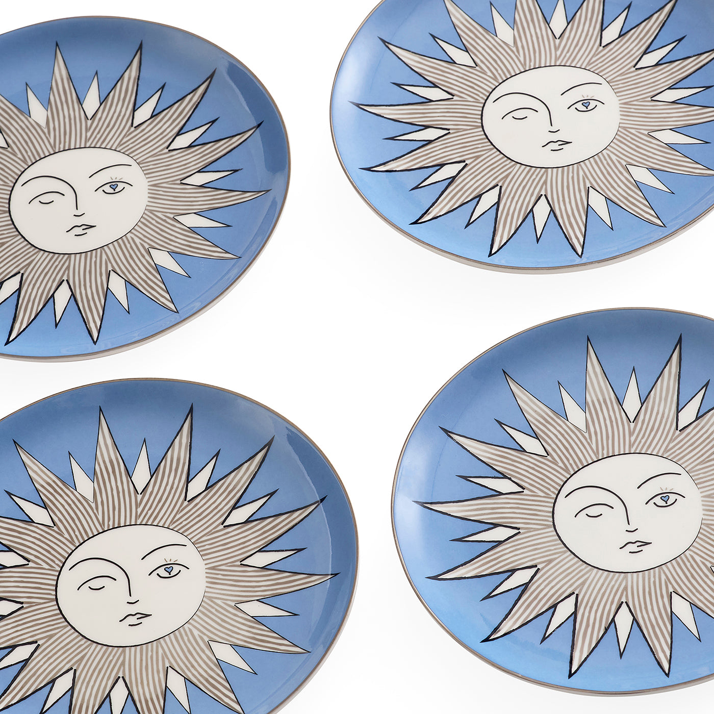 Four round ceramic plates arranged in a 2x2 grid on a white background. Each plate features a light blue border and a central white sun face design with gray rays outlined in black.