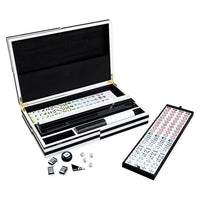 Open mahjong set with a black-and-white carrying case, a long black tile holder, a backboard with tiles, and a few loose tiles and dice on a white background.