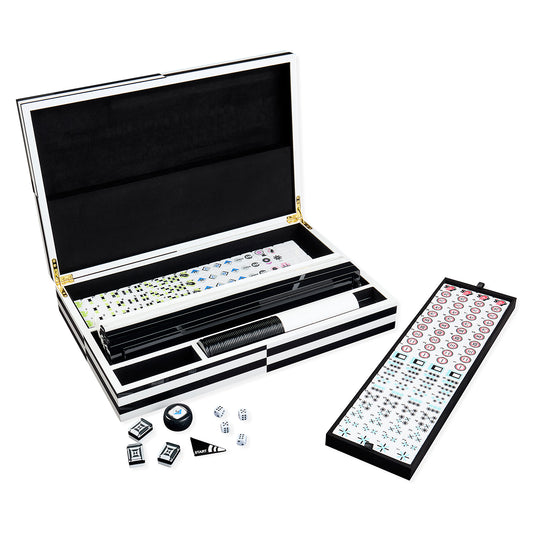 Open mahjong set with a black-and-white carrying case, a long black tile holder, a backboard with tiles, and a few loose tiles and dice on a white background.