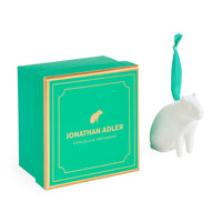 A white porcelain cat ornament next to its green and gold Jonathan Adler gift box on a white background.