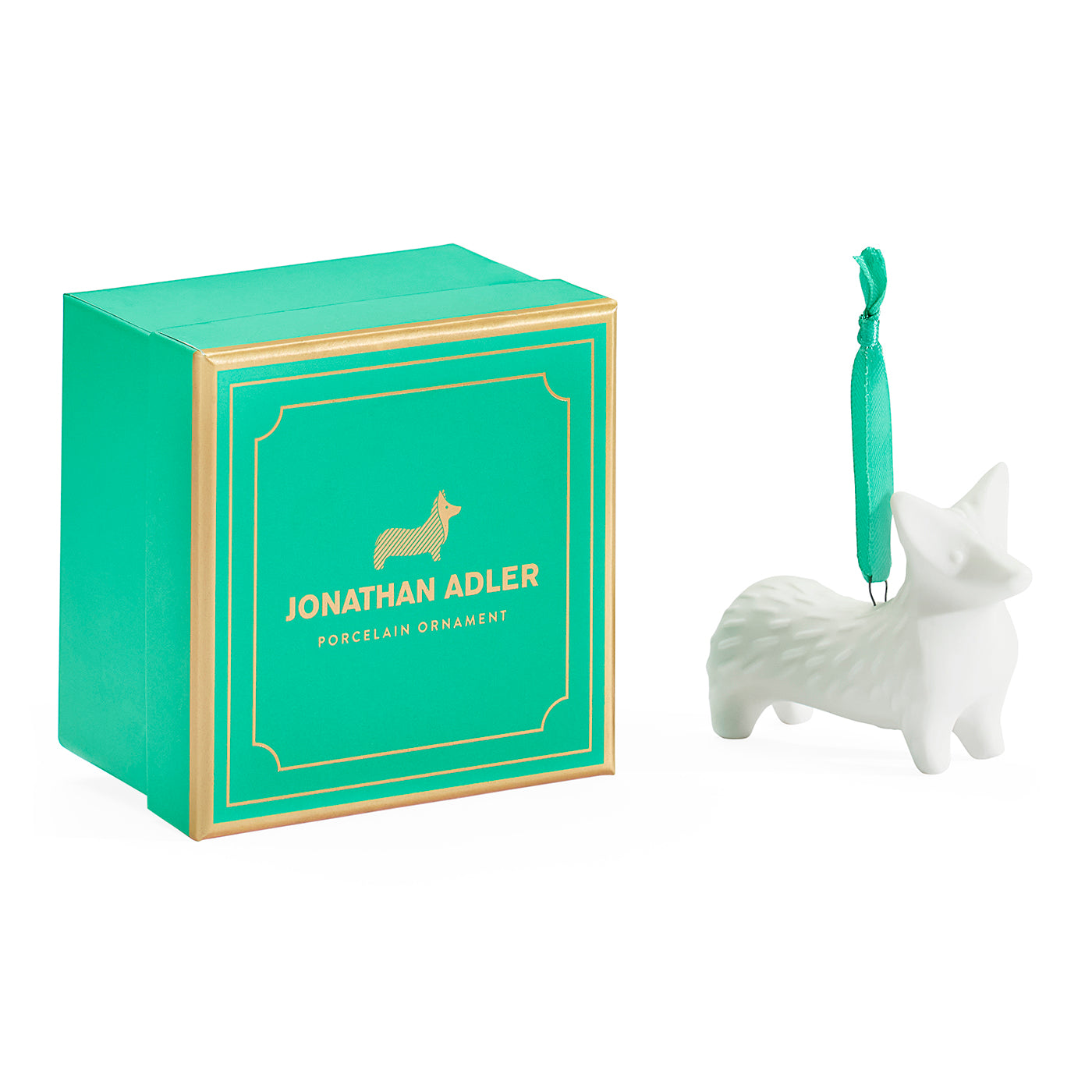 A Jonathan Adler porcelain corgi ornament in white ceramic next to its signature green and gold gift box on a clean white background.