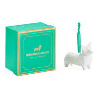 A Jonathan Adler porcelain corgi ornament in white ceramic next to its signature green and gold gift box on a clean white background.
