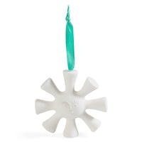 A white ceramic snowflake Christmas ornament with a small embossed face and a teal ribbon hanger, shown on a solid white background.