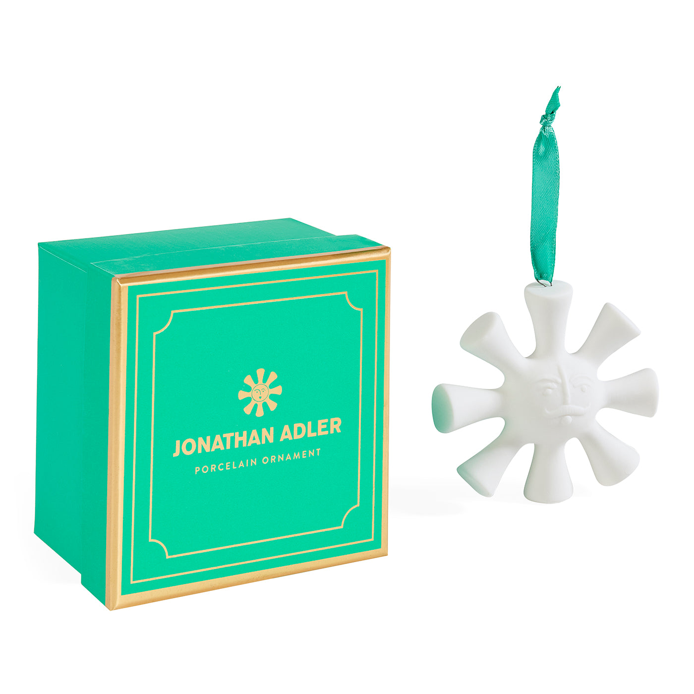 Jonathan Adler porcelain ornament shaped like a snowflake with a green ribbon loop, shown next to its signature green and gold gift box on a white background.