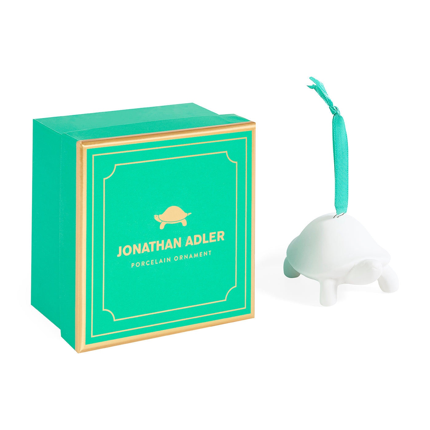 A white turtle-shaped porcelain ornament with a turquoise ribbon loop, shown next to its teal and gold Jonathan Adler gift box on a white background.