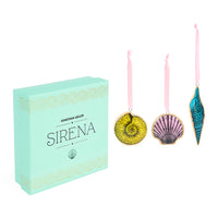 Jonathan Adler Sirena ornament set featuring a mint green gift box and three hanging seashell ornaments in yellow, pink, and blue with gold trim on a white background.