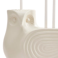 Close-up of a glossy white ceramic owl-shaped candle holder with carved owl eyes and a ribbed body, holding white candles against a bright white background.
