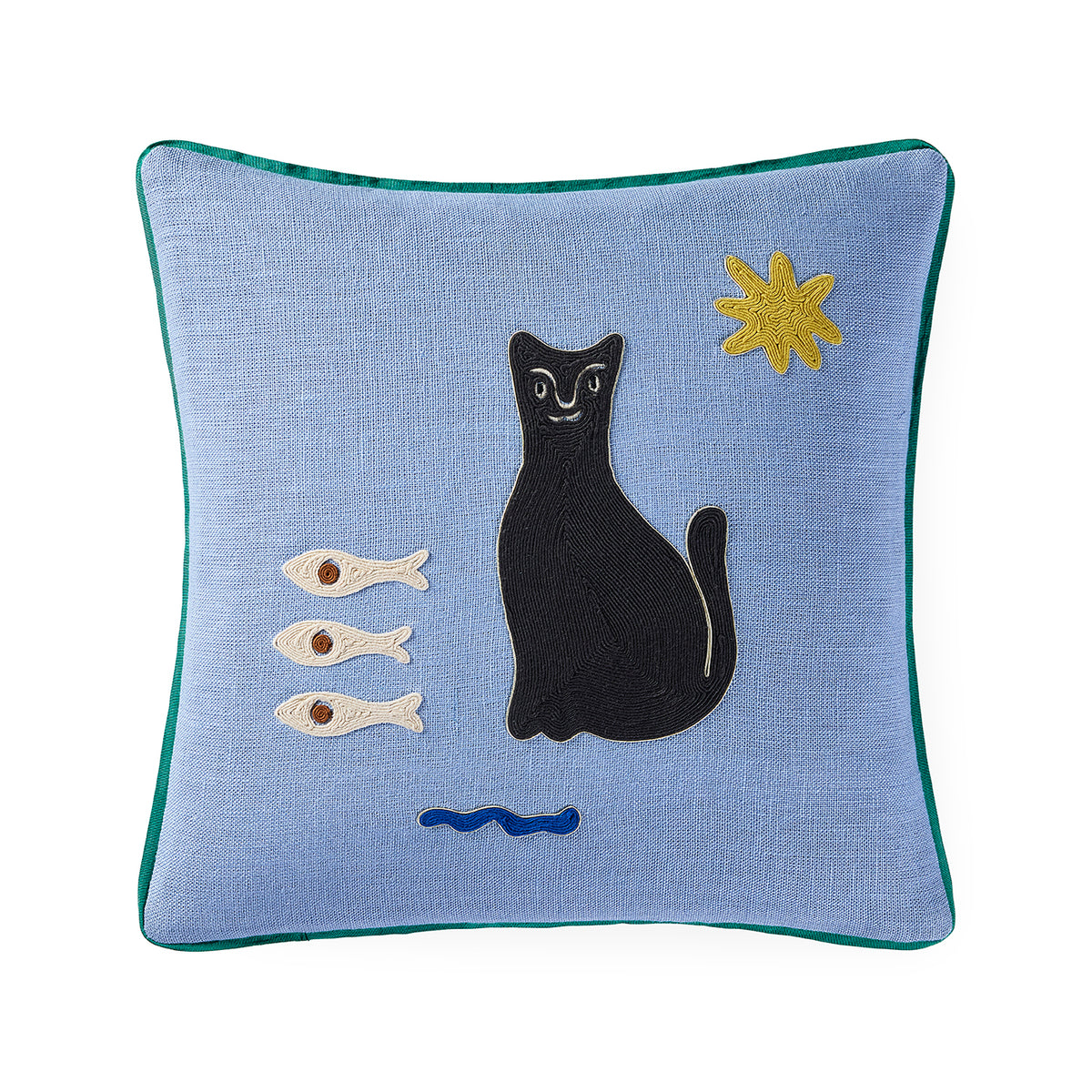 A square light blue throw pillow with a green piped edge, featuring an embroidered design of a black cat, three white fish, a blue wave, and a yellow star on a white background.