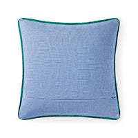 A square light blue textured throw pillow with a dark green velvet piped border, featuring a small circular embroidered monogram logo in the bottom right corner, set against a plain white background.