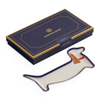 Jonathan Adler Fluffy Plush Hand Tea in a dachshund-shaped ceramic dish, shown next to its navy blue and gold presentation box on a white background.
