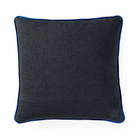 A square dark gray textured throw pillow with a vibrant blue piping border and a small circular embroidered monogram logo in the bottom right corner, set against a plain white background.