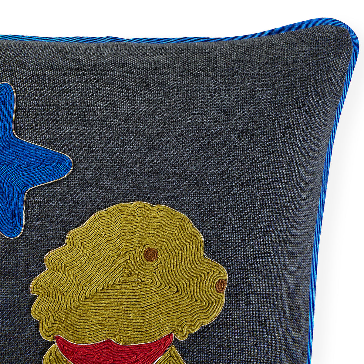Close-up of a dark gray textured throw pillow with a blue piped edge, featuring an embroidered yellow dog with a red collar and a blue star on the left.