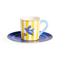 Ceramic cup and saucer with yellow and white striped design and blue bird illustration on a white background