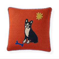 An orange textured throw pillow featuring an embroidered black and white Boston Terrier dog, a blue bone, and a yellow star on a white background.
