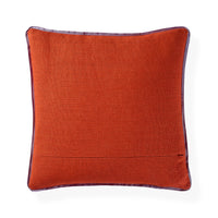 A square orange-brown textured throw pillow with a dark purple border trim and a small embroidered monogram logo in the bottom right corner, shown on a white background.