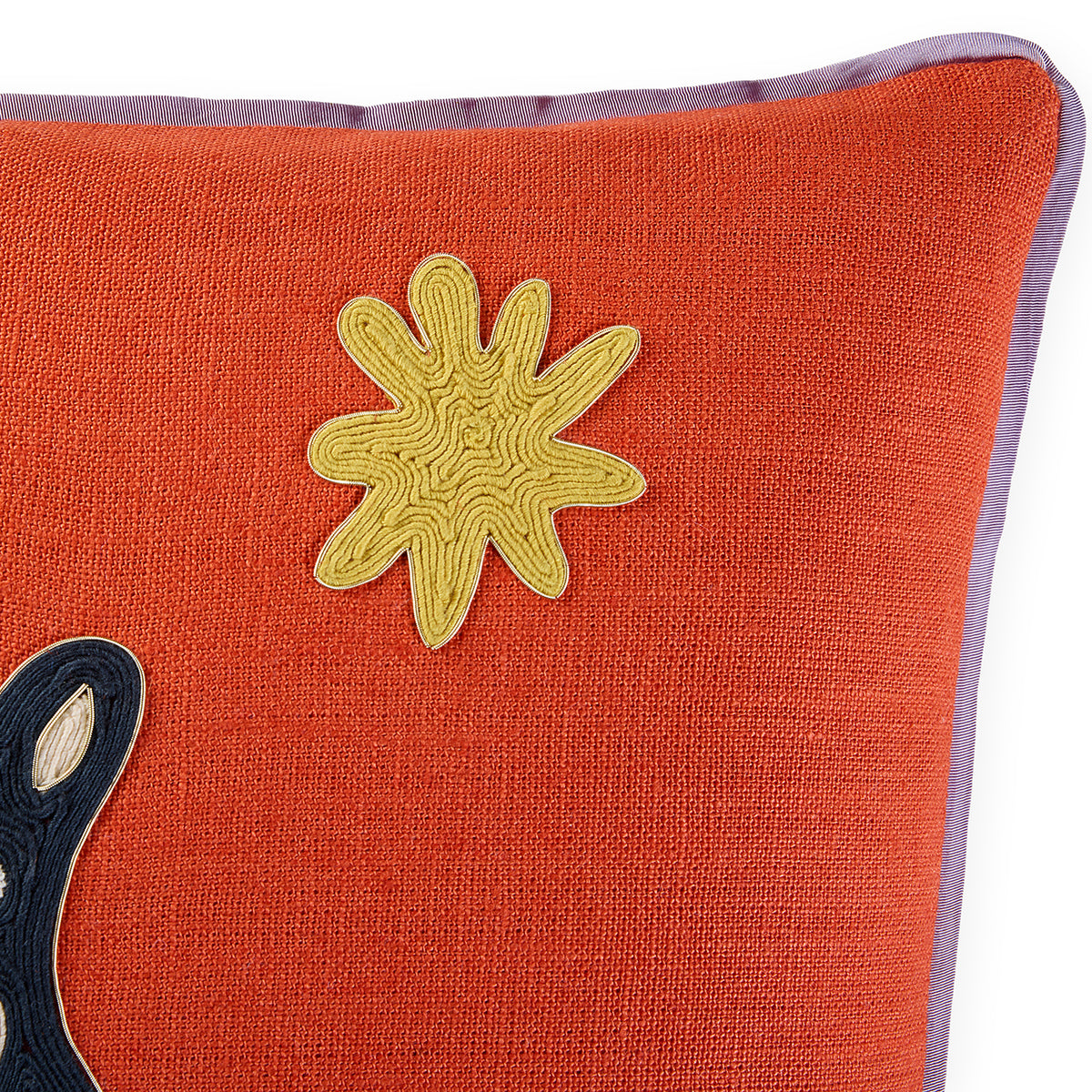Close-up of a textured orange throw pillow with a yellow embroidered starburst motif and a purple border, on a white background.