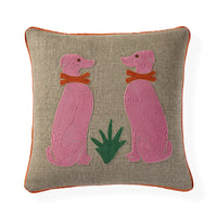 A square beige linen throw pillow with orange piping, featuring an embroidered design of two pink dogs wearing orange collars and a green plant in the center.