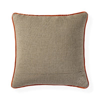 A square decorative throw pillow featuring a textured beige linen-like fabric body and a contrasting rust-orange velvet piped border, with a small circular embroidered monogram logo in the bottom right corner.