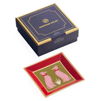 Jonathan Adler square glass dish with a red interior, gold trim, and pink dog illustrations, shown alongside its navy and gold presentation box on a white background.