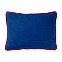 A rectangular blue lumbar pillow with a contrasting red border, featuring a subtle embroidered monogram logo in the bottom right corner, set against a plain white background.