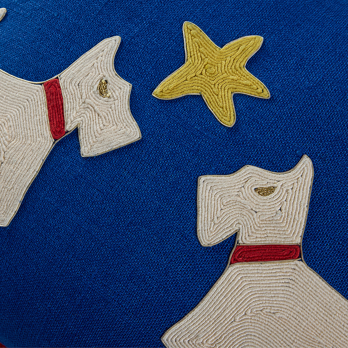 Close-up of a blue fabric surface with embroidered or appliqué dog shapes in off-white, each with a red collar, plus a yellow starfish motif.