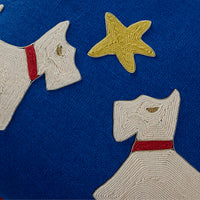 Close-up of a blue fabric surface with embroidered or appliqué dog shapes in off-white, each with a red collar, plus a yellow starfish motif.
