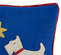 Close-up of a blue embroidered throw pillow featuring a white dog with a red collar and a yellow star, finished with a red velvet trim.