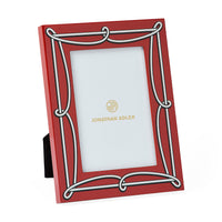 A red picture frame with an ornate white decorative border and a black stand, featuring the gold Jonathan Adler logo on the insert.