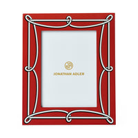 A red rectangular picture frame with an ornate white decorative border and gold Jonathan Adler branding printed in the center of the insert.