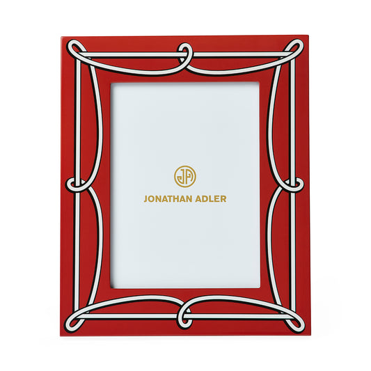 A red rectangular picture frame with an ornate white decorative border and gold Jonathan Adler branding printed in the center of the insert.