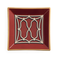 A square ceramic dish with a deep burgundy red interior, featuring a cream-colored geometric trellis pattern in the center and a thin gold rim, shown against a plain white background.