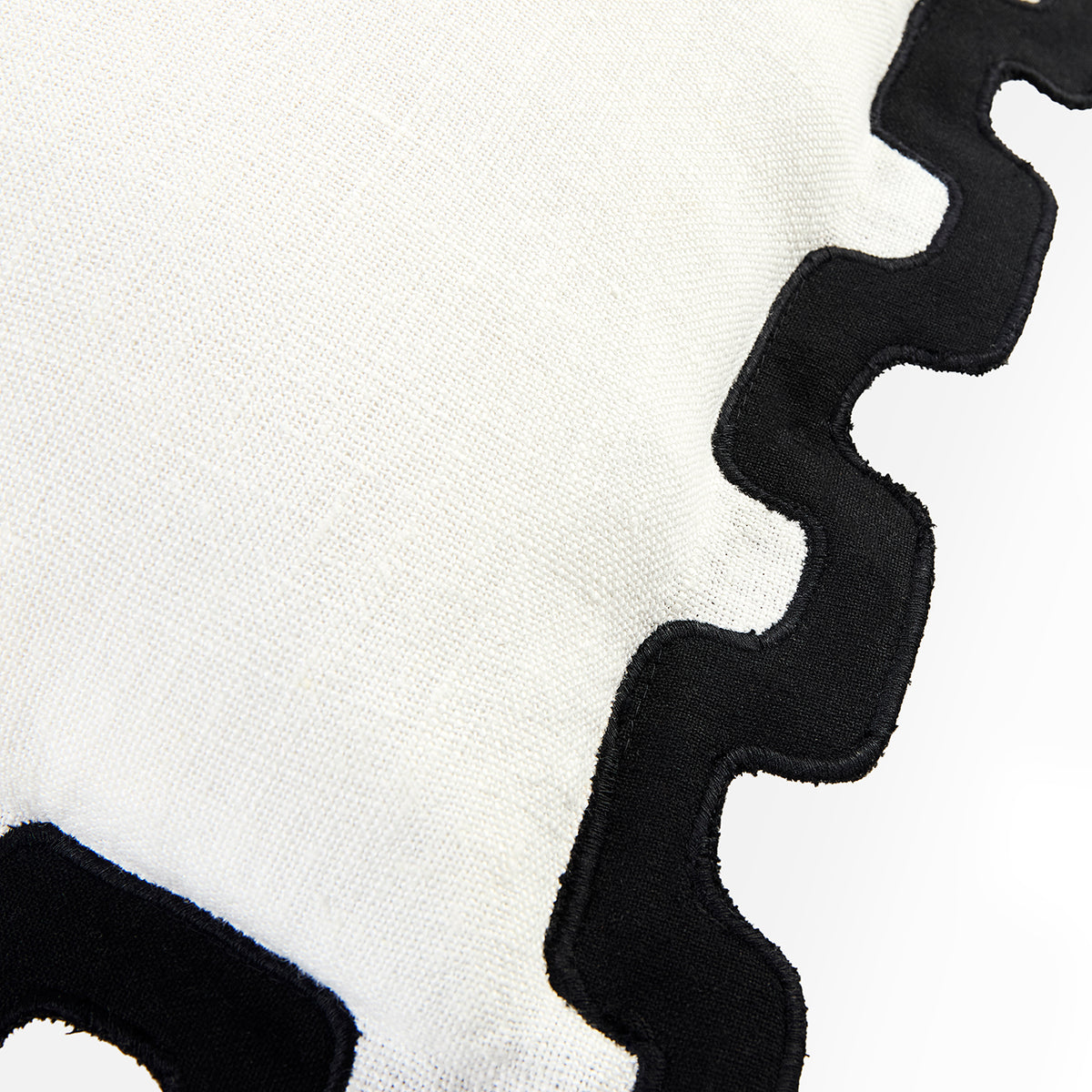 Close-up of a white textured fabric with a bold black wavy scalloped border trim.