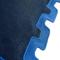 Close-up of a dark navy woven textile with a bright blue zigzag stitched border on a white background.