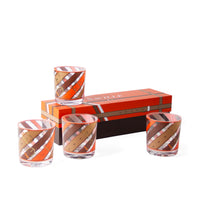 Four clear glass tumblers with an orange, brown, and white leather-strap pattern, arranged around a matching orange and brown presentation box on a white background.