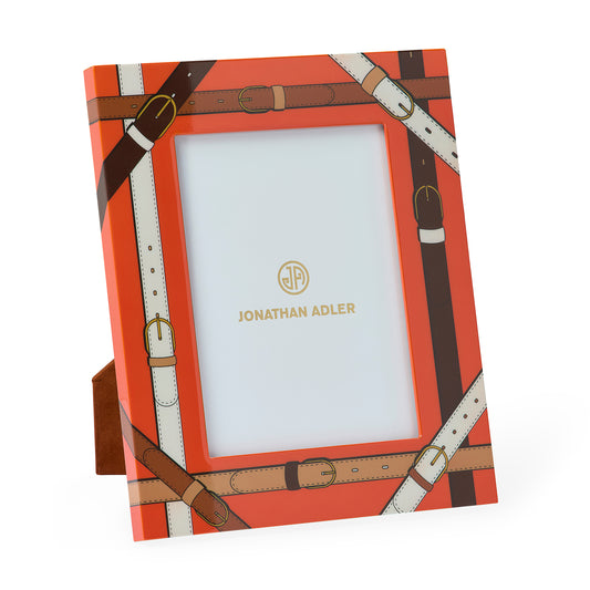 Jonathan Adler picture frame with a bright orange background and an all-over brown and cream leather-buckle print, shown standing on a small matching base against a white background.