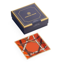 Jonathan Adler Savile Square Tray shown with its navy blue and gold presentation box on a white background. The tray features a vibrant orange background with brown leather-strap patterns and white details.