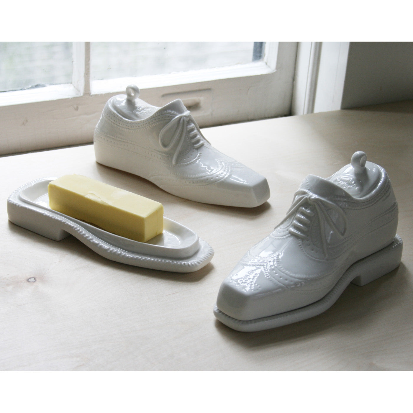 White ceramic shoes and a bar of soap on a light wooden surface with a window in the background.